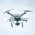 A white quadcopter drone captured flying against a clear sky, showcasing modern technology.